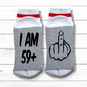 May include: A pair of gray and white socks with red stripes. One sock has the text "I AM 59+" and the other sock has a black and white illustration of a middle finger.