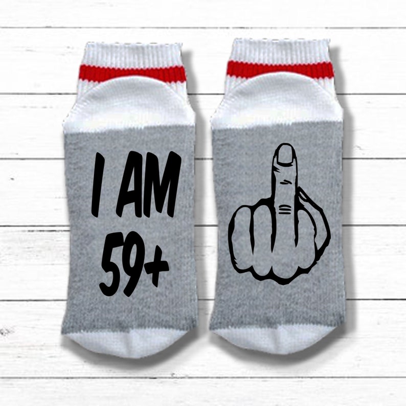 May include: A pair of gray and white socks with red stripes. One sock has the text "I AM 59+" and the other sock has a black and white illustration of a middle finger.