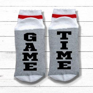 May include: A pair of gray and white socks with red stripes. One sock says "GAME" and the other says "TIME".