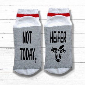 K&ouml;nnte beinhalten: Ein Paar graue und wei&szlig;e Socken mit roten Streifen. Eine Socke sagt "NOT TODAY," und die andere Socke sagt "HEIFER" mit einer Schwarzwei&szlig;-Kuh-Illustration.