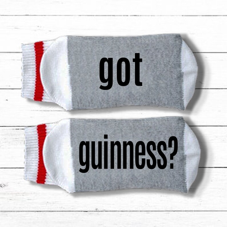 K&ouml;nnte beinhalten: Ein Paar graue Socken mit roten und wei&szlig;en Streifen. Die Socken haben den Text "got guinness?" aufgedruckt.