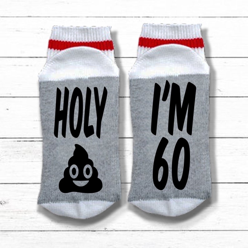 May include: A pair of white socks with red and white stripes at the top. One sock says "HOLY" with a poop emoji and the other sock says "I'M 60".