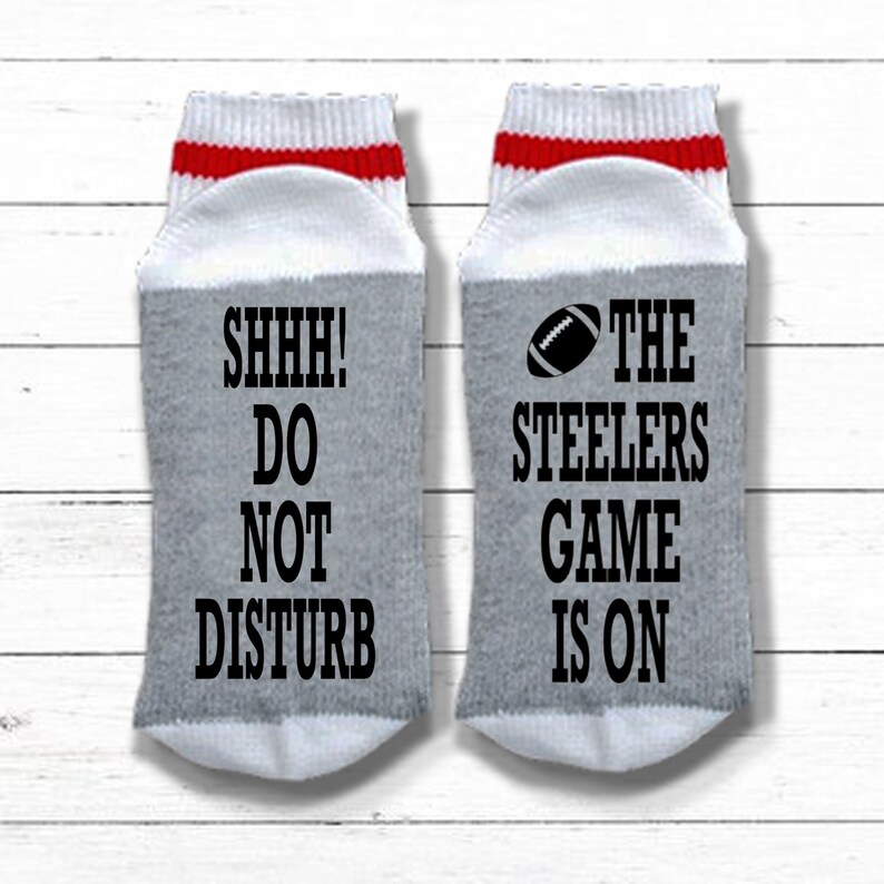 May include: A pair of gray and white socks with red stripes. One sock says "SHHH! DO NOT DISTURB" and the other says "THE STEELERS GAME IS ON" with a football graphic.