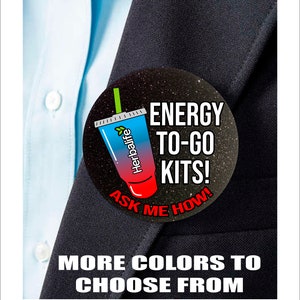 May include: A black and white button with a red, white, and blue cartoon drink with the text "Herbalife" on it. The button also has the text "ENERGY TO-GO KITS! ASK ME HOW!" in white text.
