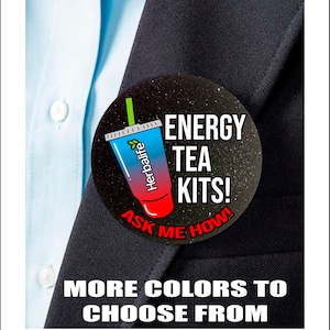 May include: A black and white button with a red and blue cartoon image of a drink with the text "ENERGY TEA KITS! ASK ME HOW!" on a black background with white glitter.