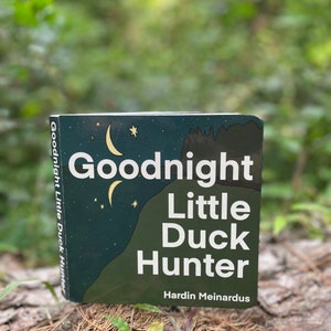 May include: A green book with the title "Goodnight Little Duck Hunter" by Hardin Meinardus. The cover features a crescent moon and stars against a dark green background.