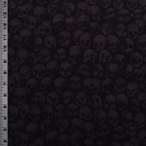 May include: A black fabric featuring a dense, repeating pattern of dark gray skulls. A ruler is visible along the left and bottom edges, showing a scale of 15 inches vertically and 12 inches horizontally, indicating the size of the skull print.