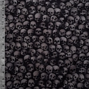 May include: A black fabric featuring a dense, repeating pattern of realistic human skulls in shades of grey and white. A white ruler with black markings is visible along the left and bottom edges, measuring up to 15 inches and 12 inches.