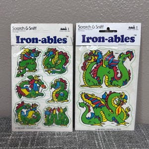 May include: Two packages of vintage "Iron-ables" scratch and sniff stickers. Each package features colorful dragon designs in green, red, yellow, and blue. The packaging includes the text "Scratch & Sniff" and "Iron-ables".