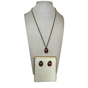 Peut inclure: Un ensemble de bijoux composé d'un collier et d'une paire de boucles d'oreilles. Le collier présente un pendentif en forme de coccinelle sur une chaîne dorée. Les boucles d'oreilles assorties sont en émail rouge avec des têtes noires.