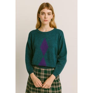 May include: Teal crew neck jumper featuring a purple diamond design. The long-sleeved jumper is worn with a green plaid skirt. The model is wearing silver hoop earrings.