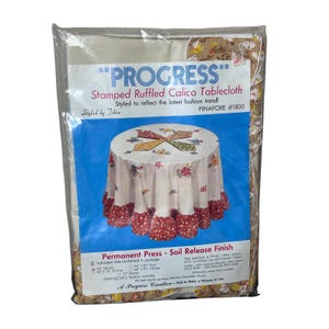 May include: A packaged "PROGRESS" stamped ruffled calico tablecloth. The package features a picture of the tablecloth with a floral design and a red ruffled edge. The text on the package says "Styled to reflect the latest fashion trend!" and "PINAFORE #1800".