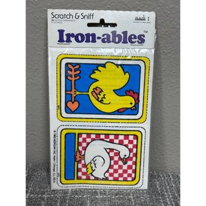Op de afbeelding: Vintage "Iron-ables" kras-en-ruik patches. De verpakking bevat twee rechthoekige patches met cartoonafbeeldingen van een haan en een gans. De haan is geel met een rode kam en de gans is wit. De patches zijn omlijst in blauw en geel.