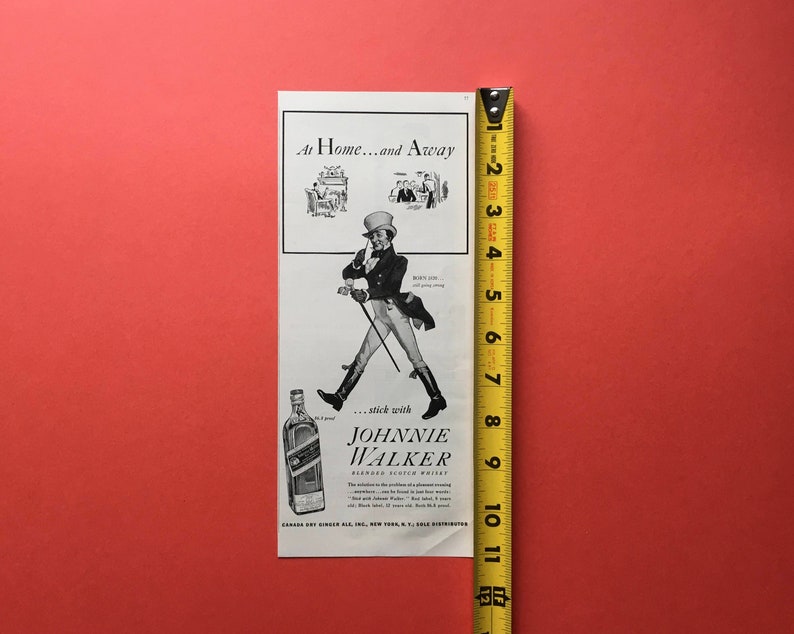 Puede incluir: Anuncio impreso en blanco y negro para Johnnie Walker Blended Scotch Whisky. El anuncio presenta a un hombre con un sombrero de copa y un bast&oacute;n, con el texto "At Home...and Away...stick with Johnnie Walker".