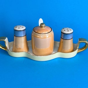 May include: A set of three vintage salt and pepper shakers with a matching tray. The shakers are peach colored with blue and gold accents. The tray is white with gold trim.