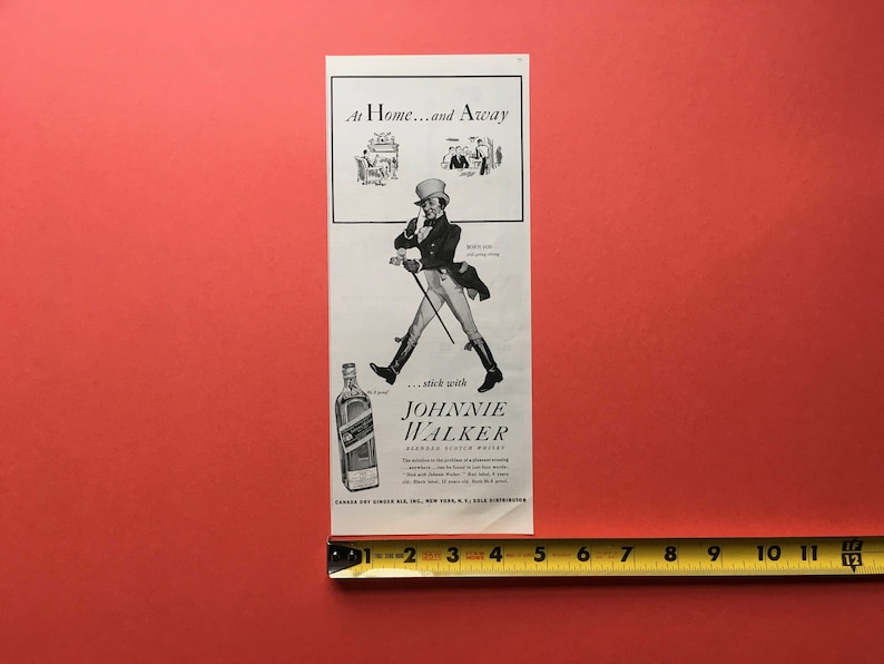 Puede incluir: Un anuncio vintage en blanco y negro para Johnnie Walker Scotch Whisky. El anuncio presenta a un hombre con un sombrero de copa y un bast&oacute;n, con una botella de Johnnie Walker en primer plano. El texto dice "At Home...and Away...stick with Johnnie Walker Scotch Whisky".