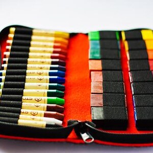 May include: A red zippered case with a black interior holds a set of 30 crayons. The crayons are arranged in two rows, with the first row containing 15 crayons and the second row containing 15 crayons. The crayons are all different colors, including red, orange, yellow, green, blue, purple, and brown.