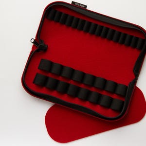 May include: Red felt zippered case with black elastic loops for holding small items. The case is open and the inside is lined with black felt. The case has a label that says "100% Woolen".