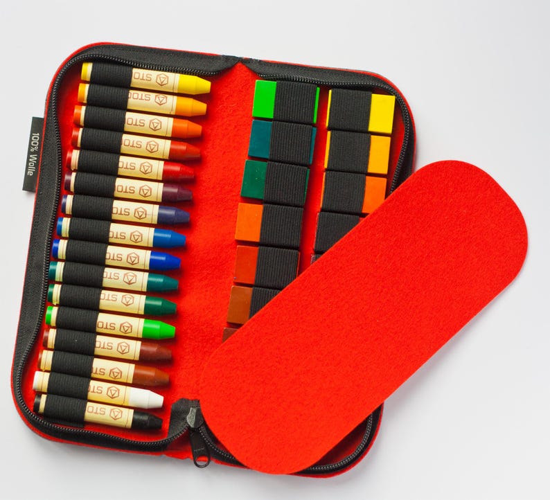 May include: A red zippered case with a felt lining. The case contains a set of colored crayons and a set of colored blocks. The case is labeled "100% Wolle".