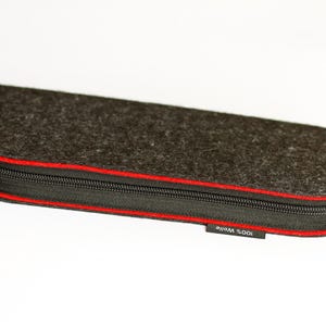 May include: A black felt pencil case with a red zipper and the text "100% WOOL" on the bottom.