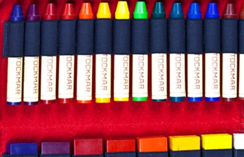 May include: A set of 12 crayons in a variety of colors, including red, orange, yellow, green, blue, purple, and brown. The crayons are arranged in a row and are labeled "TOCKMAR" on the side.