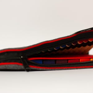 May include: A gray felt pencil case with a red zipper and a red lining. The case is open and filled with colored pencils.