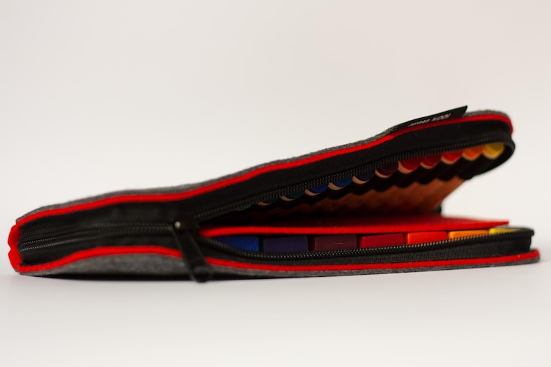 May include: A gray felt pencil case with a red zipper and a red lining. The case is open and filled with colored pencils.