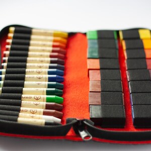 May include: A red zippered case with a black zipper pull holds a set of 24 crayons. The crayons are arranged in two rows, with 12 crayons in each row. The crayons are a variety of colors, including red, orange, yellow, green, blue, purple, and brown. The case is made of a durable material and is perfect for storing and transporting crayons.