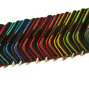 May include: A row of 17 felt pencil cases in various colors, including purple, teal, blue, red, orange, yellow, green, and black. Each case has a zipper closure and a small metal tag with the word "remarkable" printed on it.