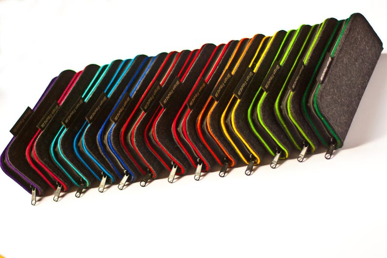 May include: A row of 17 felt pencil cases in various colors, including purple, teal, blue, red, orange, yellow, green, and black. Each case has a zipper closure and a small metal tag with the word "remarkable" printed on it.