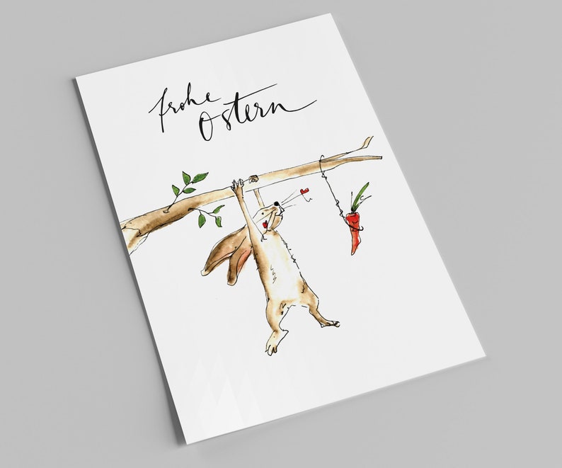 Puede incluir: Una tarjeta blanca con el texto "Frohe Ostern" escrito en cursiva negra. Un conejito de dibujos animados cuelga boca abajo de una rama, tratando de alcanzar una zanahoria que cuelga de una cuerda.