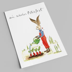 Könnte beinhalten: Aquarellillustration eines Hasen, der Karotten in einem Garten gießt. Der Hase trägt ein blau-weiß gestreiftes Hemd und eine rote Latzhose. Die Karte trägt den Text "ein schönes Osterfest" in Schreibschrift.