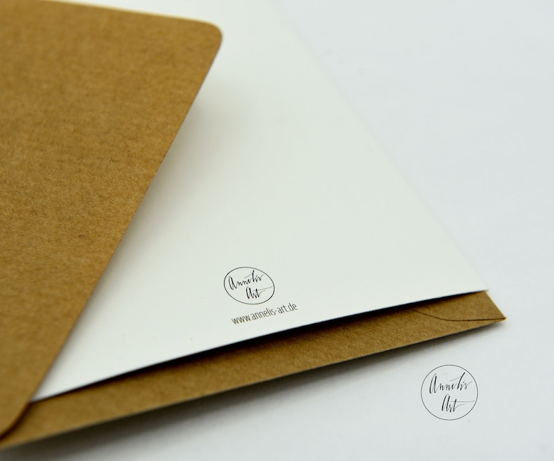 May include: A white card with a brown envelope. The card has a black circle with the text "Annelies Art" and the website address "www.annelies-art.de".