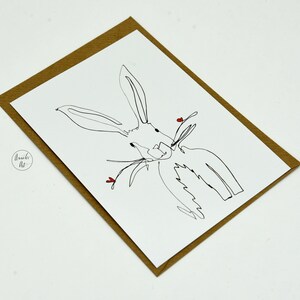 May include: A simple line drawing of a white rabbit with red hearts on a white card with a brown paper envelope.