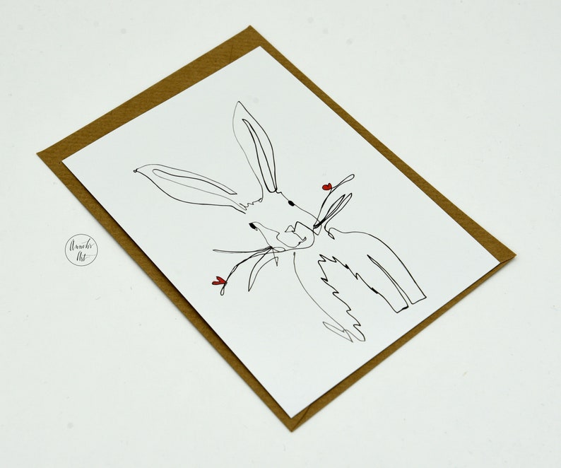 May include: A simple line drawing of a white rabbit with red hearts on a white card with a brown paper envelope.