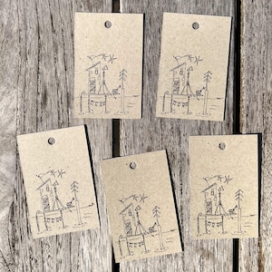 Könnte beinhalten: Fünf rechteckige Kraftpapieranhänger mit einem kleinen Loch oben. Jeder Anhänger zeigt eine handgezeichnete Illustration eines Gebäudes auf einem Pier mit Flaggen und Bäumen. Die Anhänger sind auf einer Holzoberfläche angeordnet.