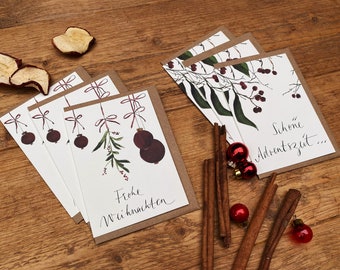 May include: Set of five Christmas cards with a brown kraft paper backing. The cards feature a watercolour illustration of a sprig of greenery with red berries and ornaments. The text on the cards reads "Frohe Weihnachten" and "Schöne Adventszeit..."