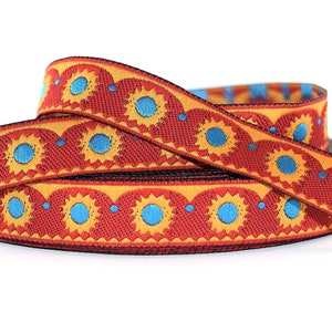 Könnte beinhalten: Rotes, gelbes und blaues gemustertes Band mit einem sich wiederholenden Muster aus stilisierten Sonnen. Das Band ist zu einer Schleife gefaltet.