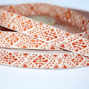 Könnte beinhalten: Eine Rolle cremefarbener Band mit einem sich wiederholenden orangefarbenen geometrischen Muster.