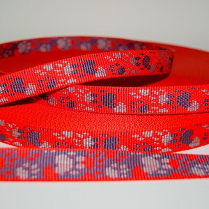 Puede incluir: Cinta roja con un patr&oacute;n repetido de huellas de patas en plata y morado.