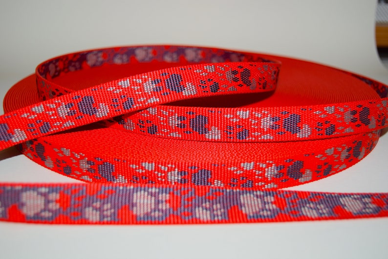 Puede incluir: Cinta roja con un patr&oacute;n repetido de huellas de patas en plata y morado.