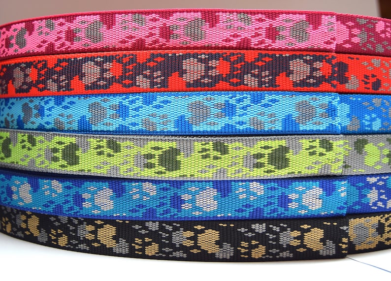 Puede incluir: Una pila de seis correas de tejido de colores con un dise&ntilde;o de huella de pata. Las correas son en tonos de rosa, rojo, azul, verde, azul claro y negro.