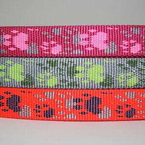 Puede incluir: Tres rollos de cinta de correa para perro de colores vivos con dise&ntilde;os de huellas de patas. El rollo superior es rosa con huellas de patas blancas, el rollo del medio es gris con huellas de patas verdes y el rollo inferior es rojo con huellas de patas negras.