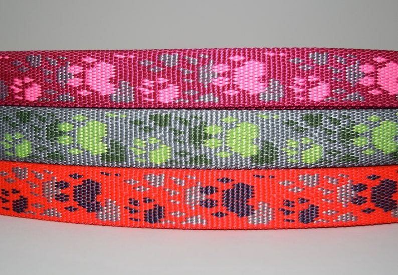 Puede incluir: Tres rollos de cinta de correa para perro de colores vivos con dise&ntilde;os de huellas de patas. El rollo superior es rosa con huellas de patas blancas, el rollo del medio es gris con huellas de patas verdes y el rollo inferior es rojo con huellas de patas negras.