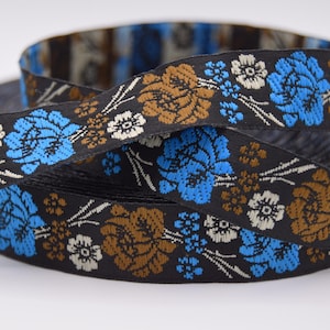 Könnte beinhalten: Schwarzes Blumenband mit blauen, braunen und weißen Blumenmustern. Das Band ist aufgerollt und zeigt das detaillierte Webmuster. Dieses dekorative Band eignet sich für verschiedene Bastelprojekte.