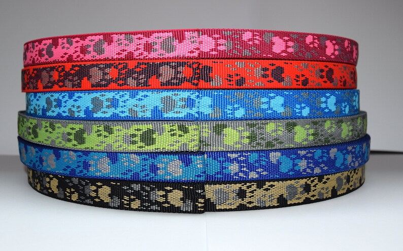 Puede incluir: Una pila de seis cintas de correa para perros de diferentes colores con un patr&oacute;n de huella de pata. Los colores son rosa, rojo, azul, verde, azul claro y negro.