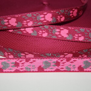 Puede incluir: Un rollo de cinta rosa y gris con un dise&ntilde;o de huella de pata. La cinta tiene aproximadamente 2,5 cm de ancho.