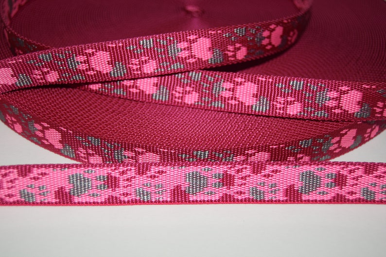 Puede incluir: Un rollo de cinta rosa y gris con un dise&ntilde;o de huella de pata. La cinta tiene aproximadamente 2,5 cm de ancho.