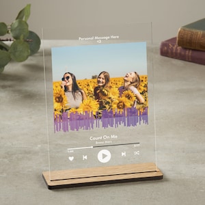 May include: Clear acrylic photo display with a wooden base. The photo shows three people in a sunflower field, with a purple sound wave graphic at the bottom. Text at the top reads "Personal Message Here <3" and "Count On Me" by Bruno Mars.