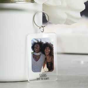 May include: A clear acrylic keychain with a photo of two women smiling. The keychain has the text "Sisters Love You Always" printed on the bottom.